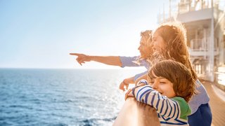Eine Familie steht an der Reling und schaut gemeinsam auf das Meer hinaus