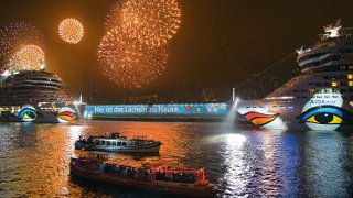 Taufe von AIDAmar Himmel ist vom bunten Feuerwerk erleuchtet, zwei AIDA Schiffe liegen im Hafen und werden von Licht angestrahlt