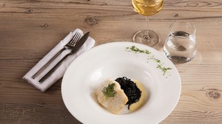 Kabeljaufilet mit schwarzem Risotto auf einem Teller