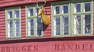 Hausfassade im Stadviertel Bryggen Rote Hausfassade mit dem Schriftzug "BRYGGEN HANDEL" und einem vergoldeten Hirschkopf