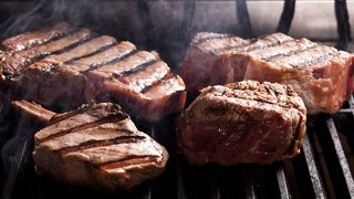Vier Steaks liegen auf dem Grill