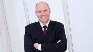 Michael Ungerer wird neuer AIDA Präsident Michael Ungerer trägt einen Anzug und blickt mit verschränkten Armen lachend in die Kamera